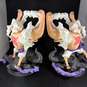 May include: A white and red figurine of a character with white hair and a white shirt. The character is standing on a black and purple base. The figurine is a popular anime character.