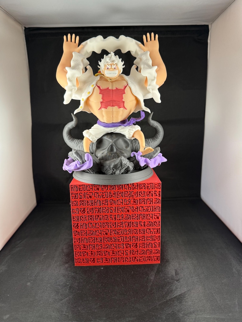 May include: A white and red anime figurine of a character with white hair and a white shirt. The character is standing on a black and purple base with a skull design. The base is on a red cube with black text.