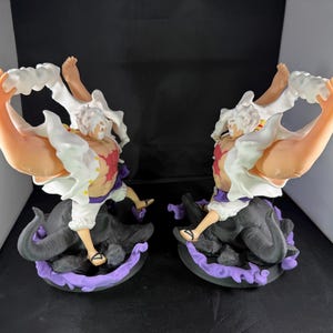May include: Two white and red anime figurines with white hair and black and purple bases. The figurines are posed with their arms raised and their hands holding white clouds.