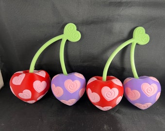 May include: Four heart-shaped cherries with green stems. The cherries are red and purple with pink hearts.