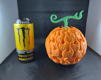 May include: A 3D printed orange and green model of the Mera Mera no Mi Devil Fruit from the anime One Piece. The fruit is next to a can of Monster Rehab Tea + Lemonade.