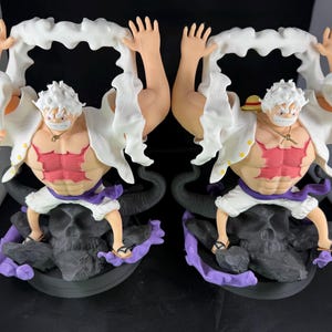 May include: Two white and red anime figurines with white hair and black and purple bases. The figurines are holding white fabric in their hands.
