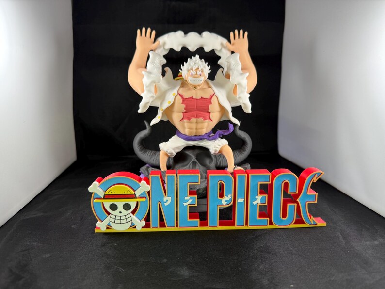 May include: A white and red figure with white hair and a white shirt with a red design is sitting on a black figure with horns. The figure is holding a white cloud in each hand. The figure is sitting on a red and blue "ONE PIECE" sign with a skull and crossbones logo.