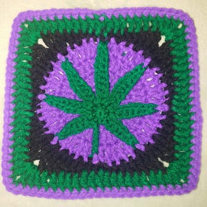 Könnte beinhalten: Ein quadratischer, gehäkelter Artikel mit einem Cannabisblatt-Design. Das zentrale Blatt ist grün, vor einem lila Hintergrund. Das Design wird von schwarzen und grünen Rändern mit einem lila Außenrand umrahmt.