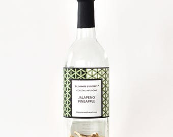 May include: A clear glass bottle with a black cap, containing cocktail infusion ingredients. The label reads "Jalapeno Pineapple" with a geometric green and white design. The bottle is filled with dried fruit and spices, perfect for making cocktails.