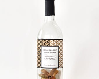 May include: A clear glass bottle with a black top and a label that reads "Spiced Old Fashioned" with the brand name "Blossom & Barrel." The bottle is filled with dried fruits, spices, and herbs, suggesting a cocktail infusion kit.