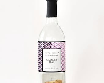 May include: A clear glass bottle with a black cap, containing cocktail infusions. The label reads "Blossom & Barrel Cocktail Infusions Lavender Pear." The bottle is filled with dried pears, berries, and other ingredients. The label has a geometric design in black and lavender.
