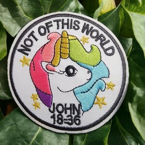 May include: A white embroidered patch with a colorful unicorn, stars, and the text "Not of this world" and "John 18:36".