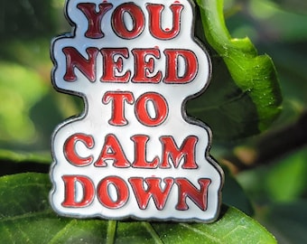 May include: White enamel pin with red lettering that reads "You Need To Calm Down".
