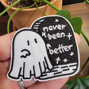 May include: White ghost embroidered patch with black outline. The ghost is next to a black tombstone with white embroidery that reads "never been better".