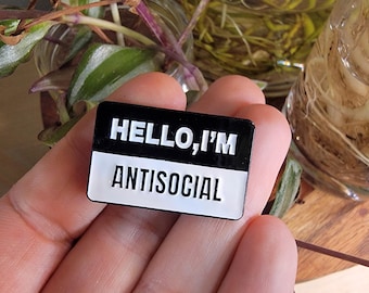 May include: Black and white enamel pin with the text "HELLO, I'M ANTISOCIAL" on it.