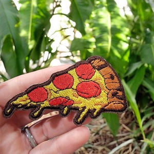 May include: A yellow and brown embroidered iron-on patch of a pizza slice with red pepperoni.