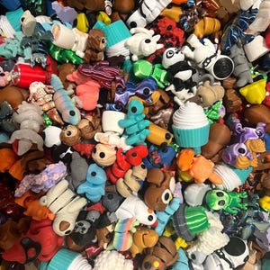 May include: A large collection of colorful, small, plastic figurines. The figurines are in various shapes and sizes, including animals, food, and abstract designs.