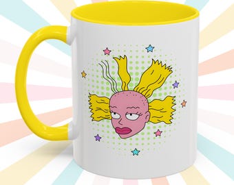 May include: White ceramic mug with a yellow handle and interior. The mug features a cartoon illustration of a character's face with yellow hair, pink skin, and a stern expression, surrounded by stars.