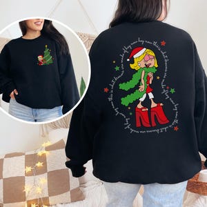 May include: Black sweatshirt with a Christmas-themed graphic of a woman wearing a red Santa hat and green scarf, standing on high heels. The text around the graphic reads "This is what dreams are made of, fly now, hey now, this is what dreams are made of, fly now, hey now".