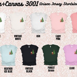 May include: A Bella+Canvas 3001 Unisex Jersey Short Sleeve Tee in ten different colors: white, vintage white, ash, light pink, pink, heather ice blue, vintage black, forest green, and lilac. Each shirt features a small graphic of a Christmas tree with a cartoon elf.