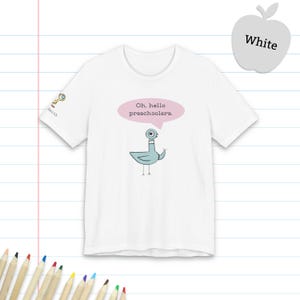 May include: A white short-sleeved t-shirt featuring a cartoon pigeon illustration in the center. Above the pigeon is a pink speech bubble containing the text "Oh, hello preschoolers." A small magnifying glass icon and the word "Smith" appear on the sleeve.