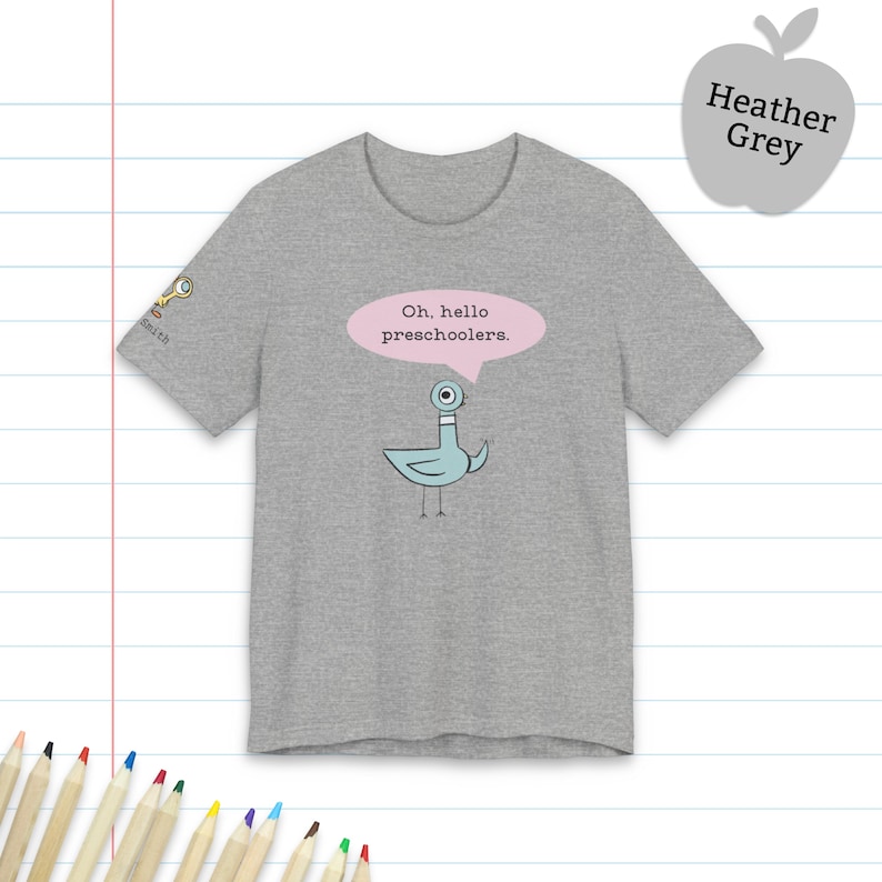 May include: A heather grey short-sleeve t-shirt featuring a light blue cartoon pigeon with a single large eye. Above the pigeon is a pink speech bubble containing the black text, Oh, hello preschoolers. A small key icon is on the sleeve.