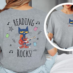 May include: Gray t-shirt with a blue cat character playing a guitar and the text "Reading Rocks!" on the back. The front of the shirt has a smaller image of the cat with the text "Ms. Wilson".