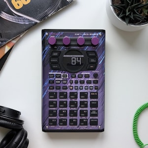 May include: A black and purple SP-404MKII sampler with a digital display showing "84". The device has numerous buttons and knobs, with the text "SP-404MKII" visible. The design incorporates purple and blue accents.