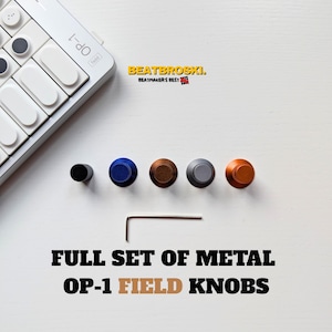 May include: A set of five cylindrical metal knobs in black, blue, brown, silver, and orange, accompanied by a small L-shaped hex key. The knobs are displayed alongside a white OP-1 synthesizer. Text reads BEATBROSKI. BEATMAKER'S BEST and FULL SET OF METAL OP-1 FIELD KNOBS.
