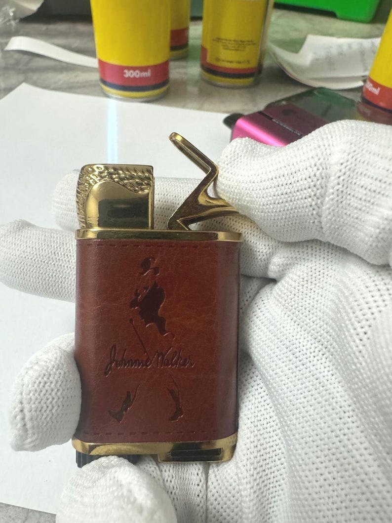 May include: A gold and brown lighter with a John Walker logo and a flame coming out of the top.
