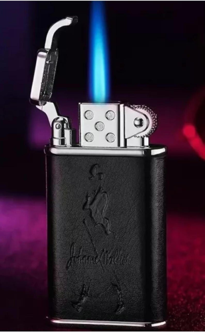 May include: A black and silver lighter with a blue flame. The lighter has a leather-like finish and the words "Johnnie Walker" embossed on the front.