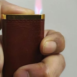 May include: A brown leather lighter with a gold trim and a blue and pink flame.