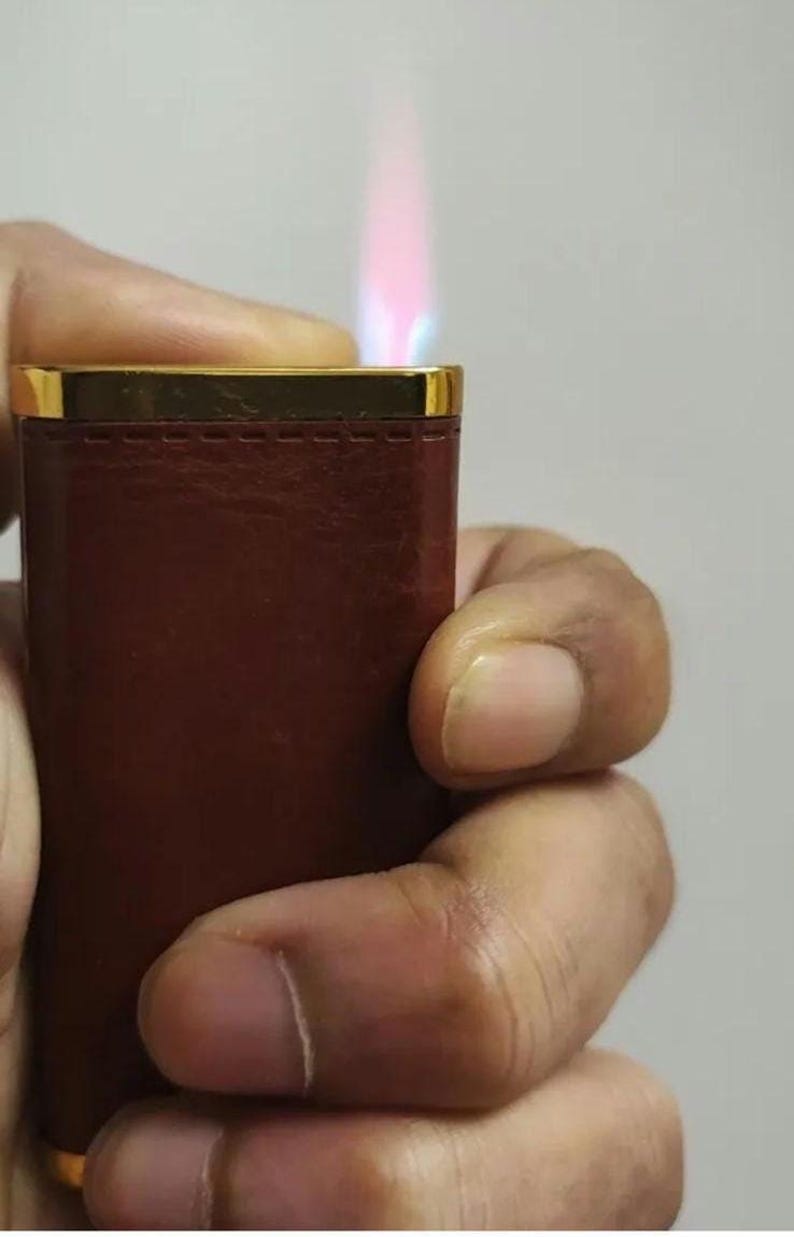 May include: A brown leather lighter with a gold trim and a blue and pink flame.