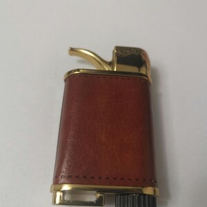 May include: A brown leather lighter with a gold trim and a gold-colored spout. The lighter has a black wheel on the bottom.