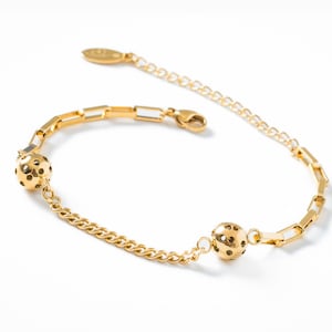 Może przedstawiać: Złoty bransoletka z dwoma okrągłymi, ażurowymi zawieszkami. Bransoletka ma wzór łańcuszkowy i zapięcie na karabińczyk.