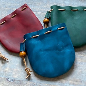 May include: Three leather pouches with drawstrings and wooden beads. The pouches are burgundy, teal, and blue.