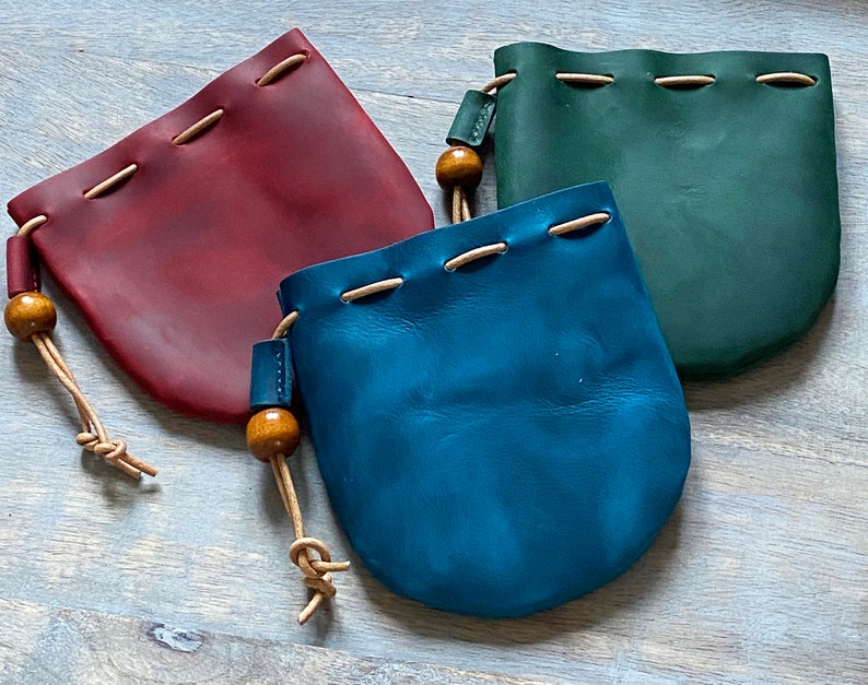 May include: Three leather pouches with drawstrings and wooden beads. The pouches are burgundy, teal, and blue.