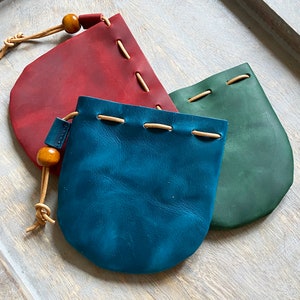 May include: Three leather pouches with drawstrings and wooden beads. The pouches are red, blue, and green.
