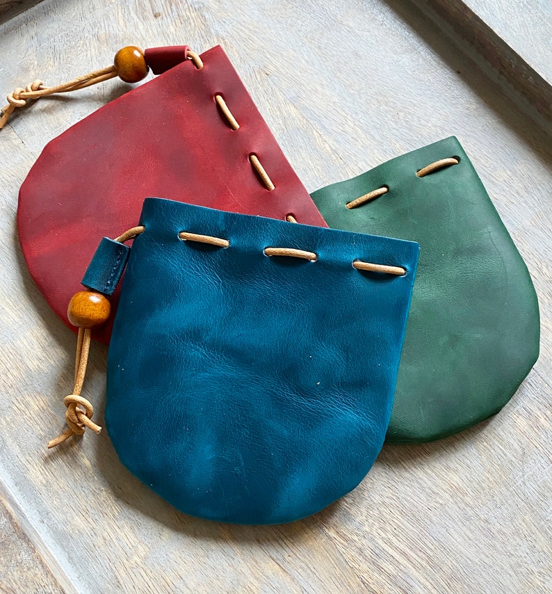 May include: Three leather pouches with drawstrings and wooden beads. The pouches are red, blue, and green.