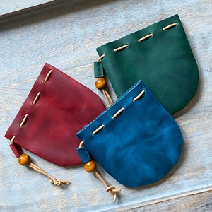 May include: Three leather pouches with drawstrings and wooden beads. The pouches are in shades of red, blue, and green.