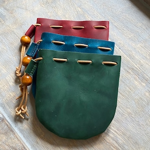 May include: Three leather pouches with drawstrings and a beaded tassel. The pouches are stacked on top of each other, with the top pouch being red, the middle pouch being blue, and the bottom pouch being green.