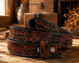 May include: A black and brown leather belt featuring an embossed sunflower and floral pattern throughout the strap. The belt includes white contrast stitching along the edges and a small leather keeper loop secured with two silver-toned metal rivets.