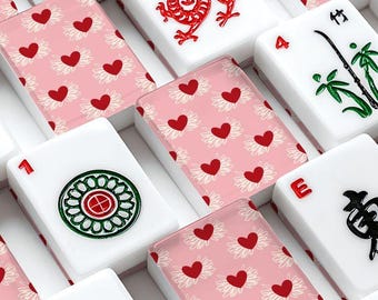 Juego de fichas de mahjong americano con diseño de corazones revoloteando en rosa claro, rojo y crema.