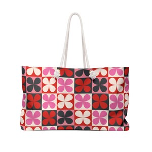 Könnte beinhalten: Große Tragetasche mit weißem Seilgriff. Die Tasche hat ein sich wiederholendes Muster aus vierblättrigen Blumen in roten, rosa, schwarzen und weißen Quadraten. Die Tasche ist zum Tragen von Gegenständen konzipiert.