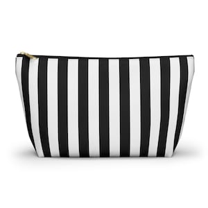 Può includere: Un beauty case a righe bianche e nere con cerniera dorata. La borsa ha strisce verticali e una forma rettangolare, adatta per riporre trucchi o articoli da toeletta. La borsa è realizzata in un materiale resistente.
