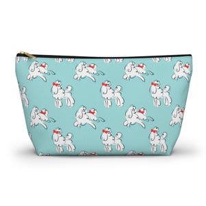 May include: A light blue cosmetic bag with a repeating pattern of white poodle illustrations wearing red bows. The bag has a gold zipper and a black zipper pull. The bag is made of a soft, durable material.