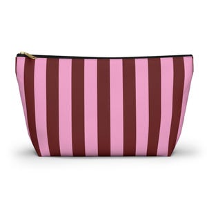 Könnte beinhalten: Eine rechteckige Kosmetiktasche mit einem vertikalen Streifenmuster in Rosa und Burgunderrot. Die Tasche hat einen schwarzen Reißverschluss und einen goldfarbenen Reißverschluss.