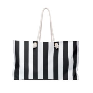 May include: A large tote bag with a black and white striped pattern. The bag has white rope handles and decorative white seashell accents. The bag is designed for carrying items and has a rectangular shape.
