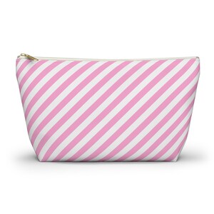 Può includere: Un beauty case a righe rosa e bianche con cerniera dorata. Le strisce diagonali creano un motivo visivamente accattivante. La borsa è progettata per contenere trucchi e altri prodotti di bellezza.