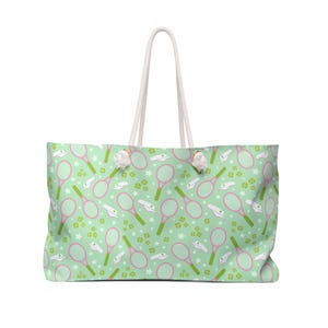 May include: A large tote bag with a light green background featuring a pattern of pink tennis rackets, tennis balls, paper airplanes, and white stars. The bag has white rope handles.