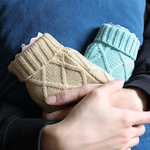 May include: Two cable-knit baby booties, one tan and one light blue, are held together. The booties have a ribbed cuff and a soft, light pink interior. The tan bootie is on the left, and the light blue bootie is on the right.