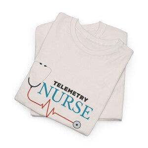 Könnte beinhalten: Weißes T-Shirt mit einer blauen Stethoskopgrafik und dem Text "Telemetry Nurse" in Blau und Rot. Das Stethoskop hat eine rote Herzschlaglinie.