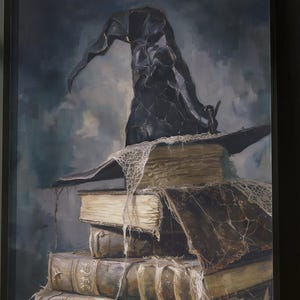 Puede incluir: Una obra de arte enmarcada representa un sombrero de bruja negro sobre una pila de libros antiguos, cubiertos de telarañas. Los libros están encuadernados en cuero marrón desgastado. El fondo presenta un cielo oscuro y melancólico, creando un tema gótico de Halloween.