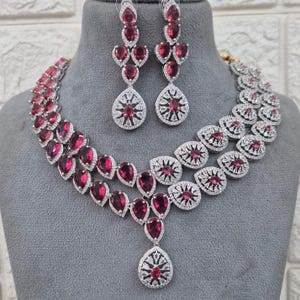 Peut inclure: Un collier et des boucles d'oreilles en argent avec une double rangée de pierres rouges en forme de goutte et un grand pendentif en forme de goutte. Le collier et les boucles d'oreilles sont ornés de pierres de zircone cubique transparentes.
